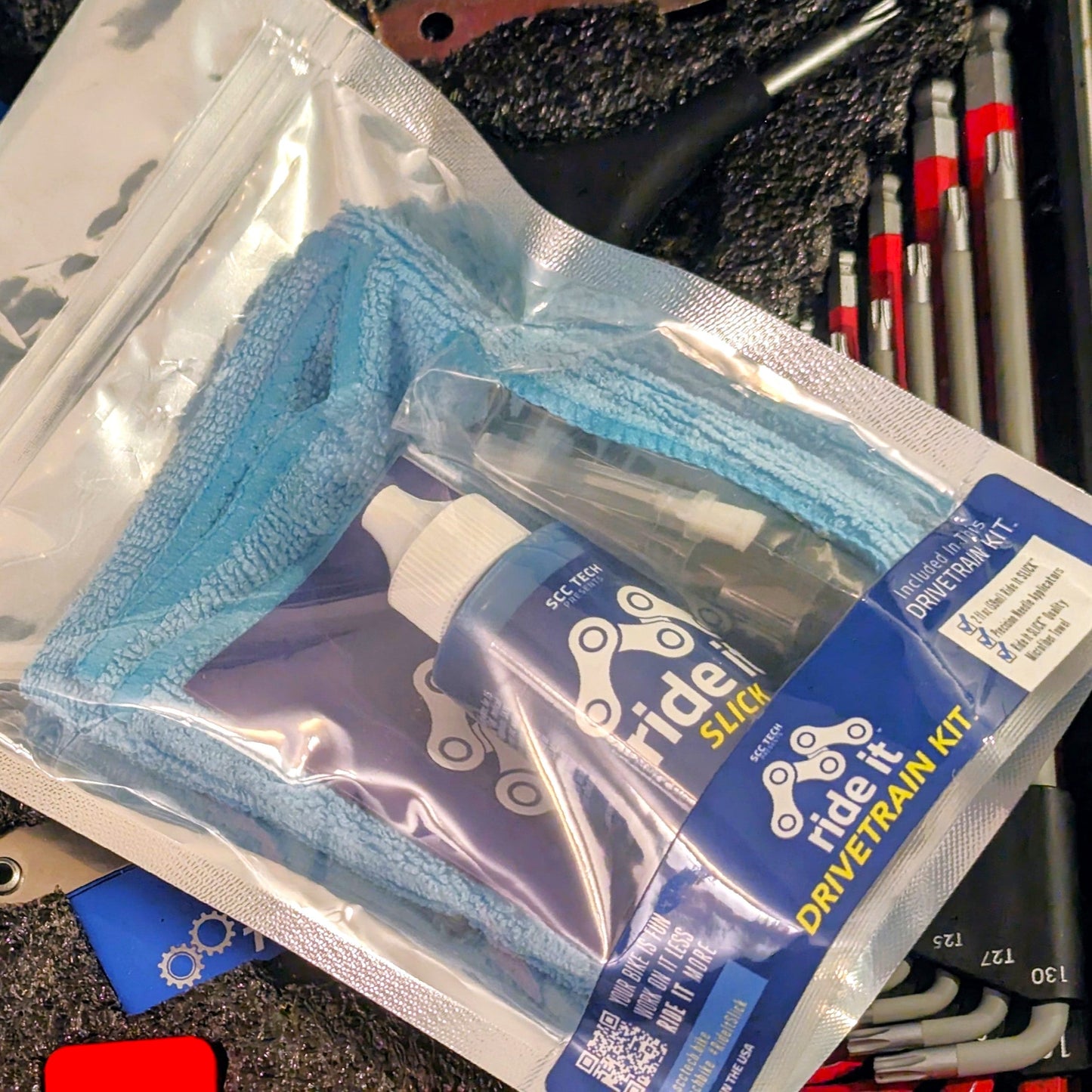 Ride It Drivetrain Kit by SCC Tech, featuring a complete bike maintenance solution. The packaging displays the Ride It brand logo and includes products like Ride It Slick, Ride It Clean, Ride It Smooth, and Ride It Flow. The kit contains 2 fl oz (59 ml) bottle of Ride It Slick drivetrain treatment, precision needle applicators, and a microfiber towel. The label highlights the kit’s focus on enhancing bike performance and protection, with bold text encouraging less time working on it and more time riding it
