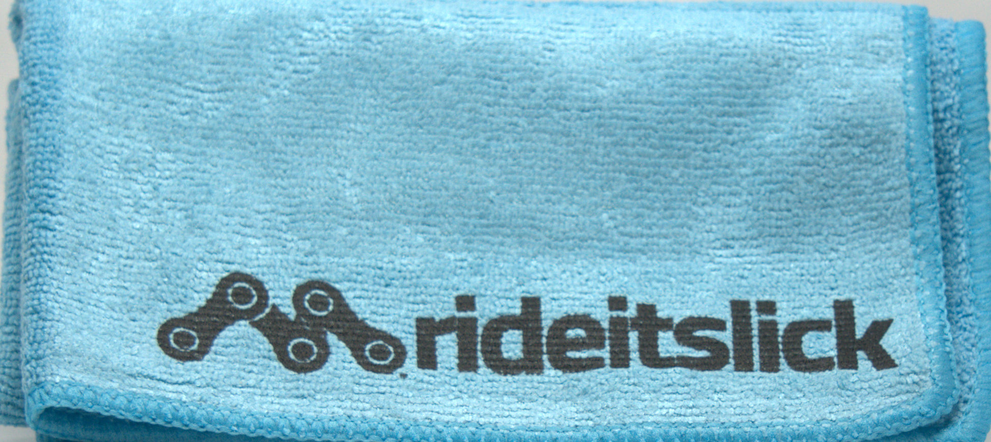 Blue microfiber towel with a printed black bicycle chain logo, designed for cleaning and maintaining bicycles. The soft, high-quality microfiber material is ideal for wiping down bike frames, components, and drivetrains, helping to remove dirt, grime, and excess lubricant during maintenance. This towel is part of the Ride It bike care kit, offering a gentle yet effective cleaning solution.