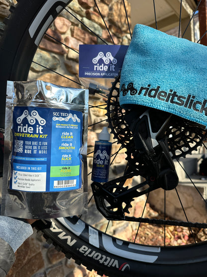 Ride It Drivetrain Kit by SCC Tech, featuring a complete bike maintenance solution. The packaging displays the Ride It brand logo and includes products like Ride It Slick, Ride It Clean, Ride It Smooth, and Ride It Flow. The kit contains 2 fl oz (59 ml) bottle of Ride It Slick drivetrain treatment, precision needle applicators, and a microfiber towel. The label highlights the kit’s focus on enhancing bike performance and protection, with bold text encouraging less time working on it and more time riding it 